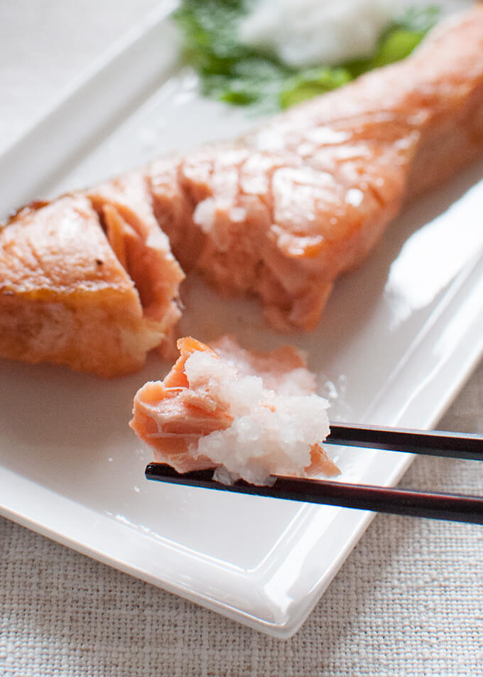 Zoomed in image of grilled salted salmon piece picked up with chopsticks.