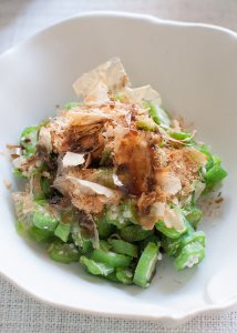 Okra in a serving bowl topped with bonito flakes and soy sauce.