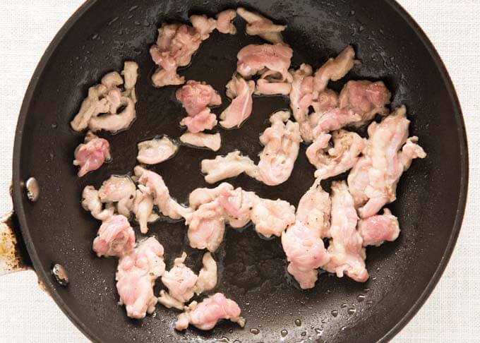 Cooking chicken neck meat in a frying pan.