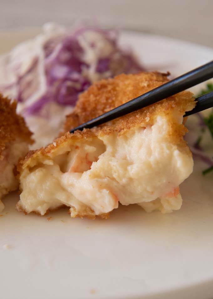 Half Creamy Shrimp Croquettes squeezed with chopsticks showing creamy béchamel inside.