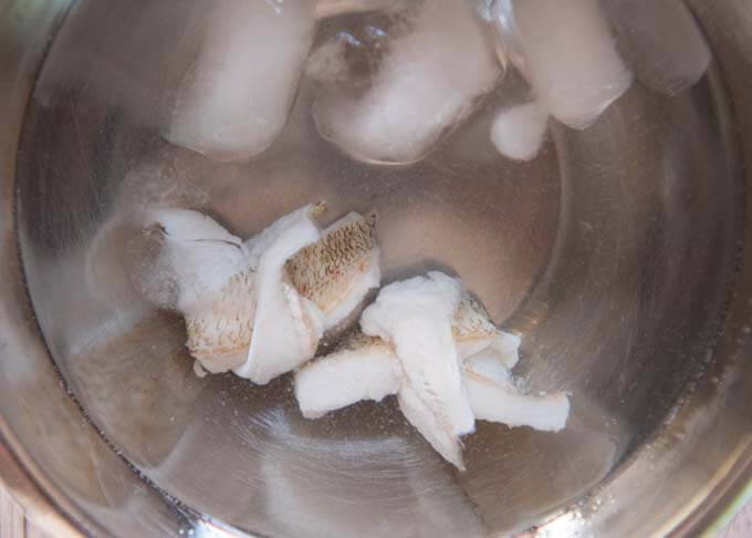 Cooling down the blanched knotted whiting fillets in ice water.