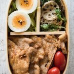 Top-down photo of Pork Shōgayaki Bento which contains Pork Shōgayaki, small tomatoes, boiled eggs on shredded lettuce and Lotus Root and Spinach salad.