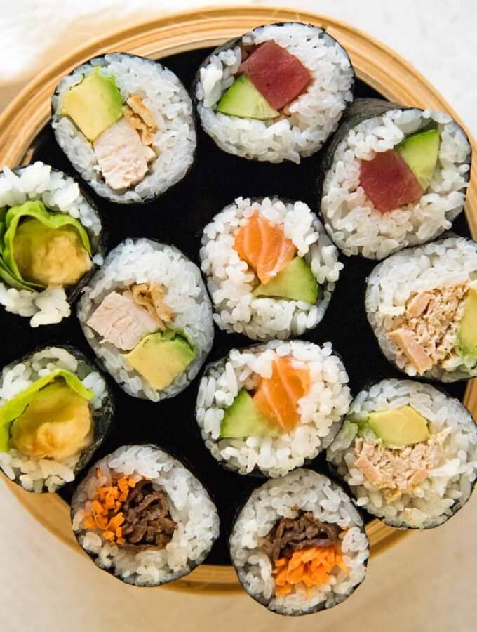 Top-down photo of 12 sushi rolls with 6 different fillings fit in a bamboo container.