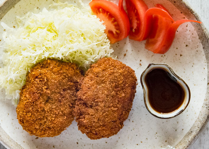 Top-down photo of Menchi Katsu on a place with sauce on the side.