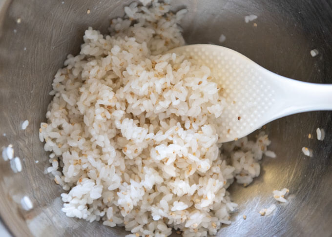 Mixing roasted white sesame seeds to the sushi rice in a bowl.