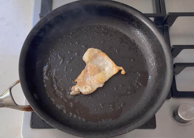 A piece of chicken skin on a hot frying pan to make chicken oil.