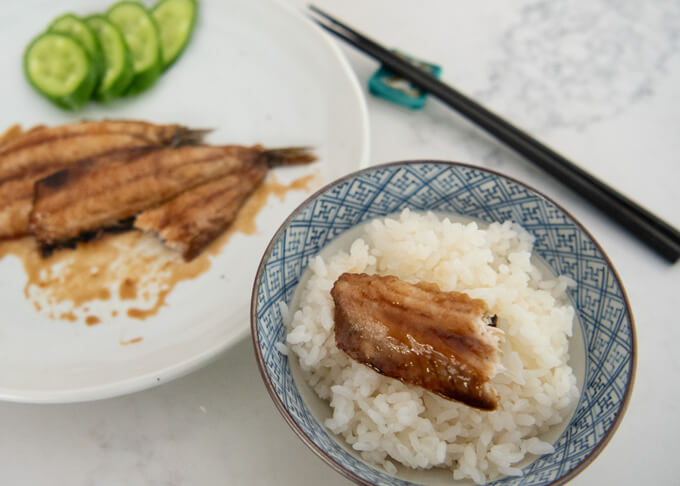 Half bitten Sardine Kabayaki on a small bowl of rice.
