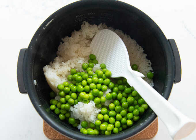 Mixing boiled green peas into the cooked rice.
